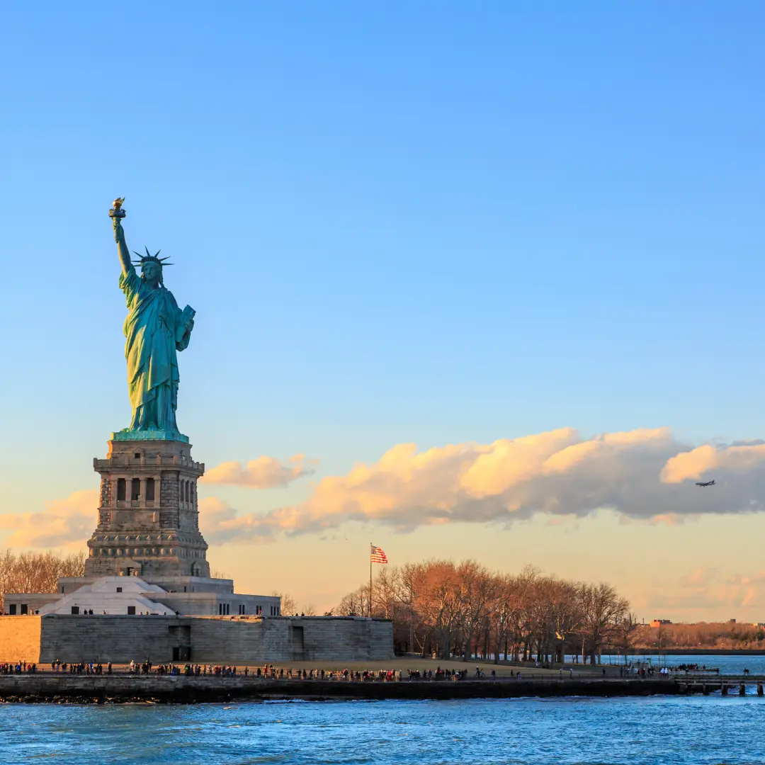 Statue of Liberty standing on Liberty Island under a clear blue sky at sunset.