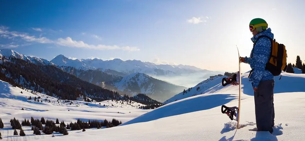 A man stood holifng his snowboard looking at the winter landscape.