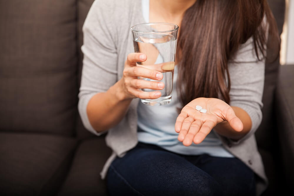 A woman holding a glass of water and pills