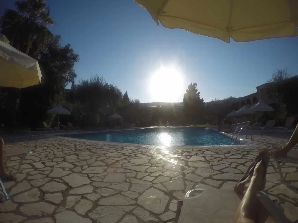 Sunny outdoor resort swimming pool surrounded by paved stone decking, lounge chairs and yellow umbrellas.