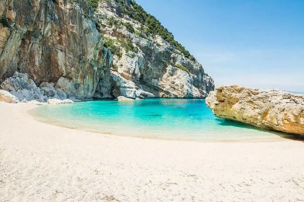 Secluded sandy cove surrounded by steep limestone cliffs and crystal-clear turquoise sea.