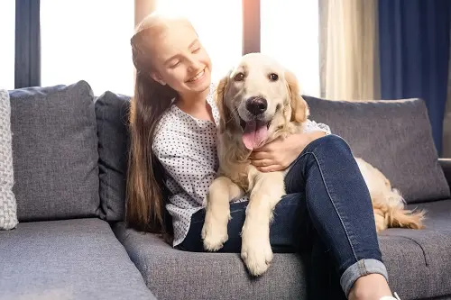 Teenager with a golden retriever on her lap sitting on a couch.