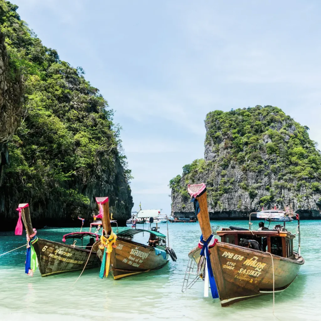 Traditional long-tail boats floating in clear turquoise water surrounded by limestone cliffs in Thailand.